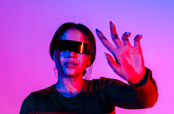 Young female in futuristic glasses gesturing stop and protecting face from bright neon light in modern room - Zdjęcie, obraz