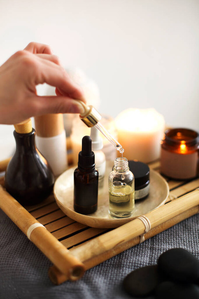 Crop masseuse using pipette with massage oil placed on tray with assorted spa supplies in salon - Foto, imagen