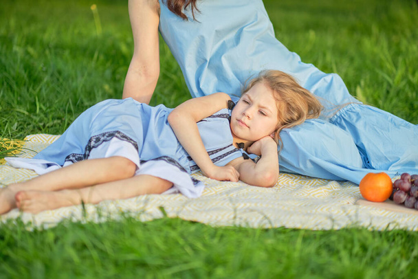 Meisje rustend op haar moeders schoot, zomer warme dag in het park. Gelukkige familie die samen rust. Geluk en harmonie in het gezinsleven. - Foto, afbeelding