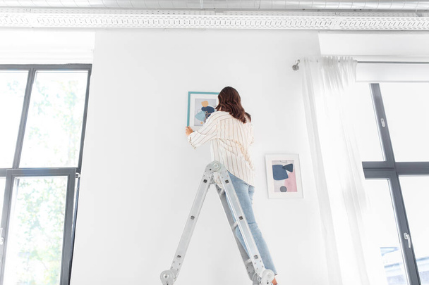 woman on ladder decorating home with art - Foto, afbeelding