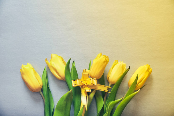 Пять желтых тюльпанов на серебряно-желтом фоне с желтой лентой и копировальным пространством - Фото, изображение