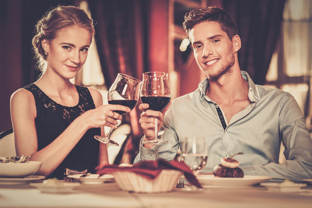 Beautiful young couple with glasses of red wine in luxury restaurant  - Photo, image