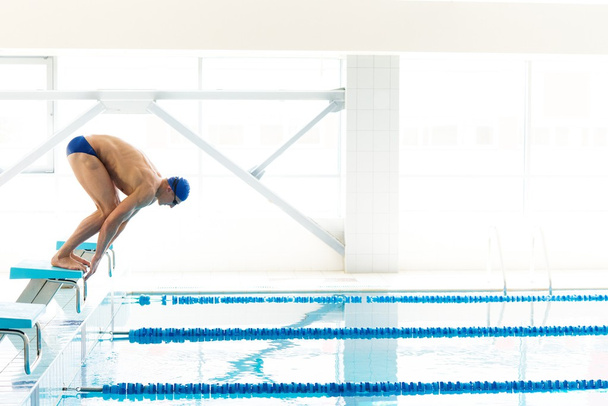 Joven nadador muscular en posición baja en el bloque de salida en una piscina
 - Foto, imagen