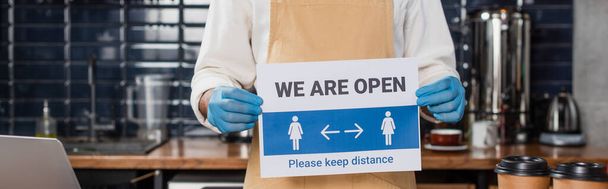 Cropped view of african american barista in latex gloves holding signboard with we are open lettering in cafe, banner  - Photo, Image