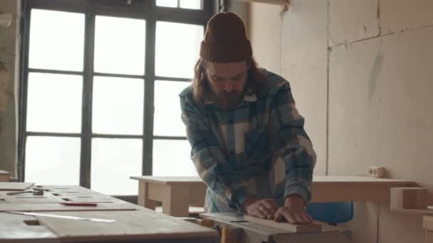Orta boy beyaz erkek marangoz kareli gömlek giyerken ve atölyedeki otomatik ahşap yönlendirici makinesinde şapka yönlendirme tahtası kullanırken. - Video, Çekim