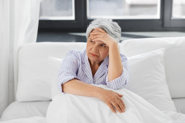 senior woman with headache sitting in bed at home - Valokuva, kuva