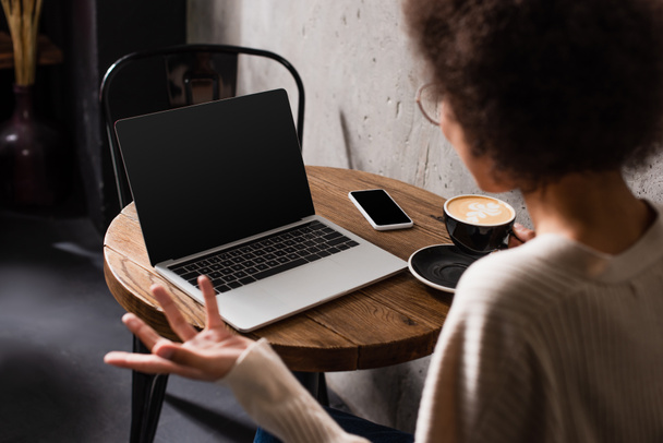 Blurred african american freelancer sitting near coffee and devices in cafe  - Фото, зображення