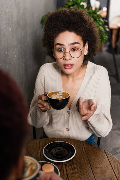 Африканская американка с кофе указывает на размытого парня в кафе  - Фото, изображение