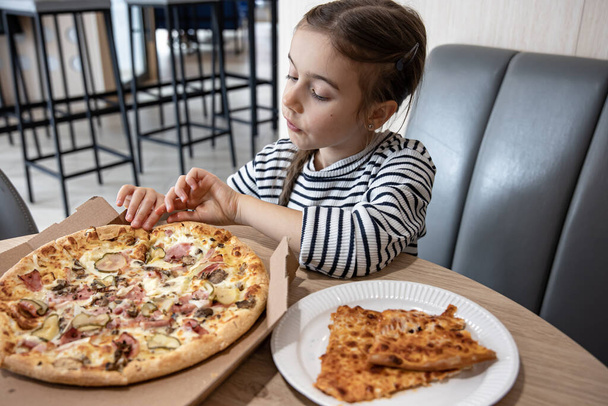 Lustiges kleines Mädchen isst Pizza in einem Karton zum Mittagessen. - Foto, Bild