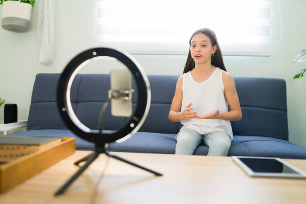 Caucasian child vlogger recording a video about the beauty trends to post on her social media channel. Influencer kid using her smartphone and a ring light at home - Photo, Image