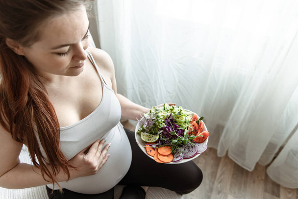 De aanstaande moeder in de laatste maanden van de zwangerschap houdt een bord groentesalade vast.. - Foto, afbeelding