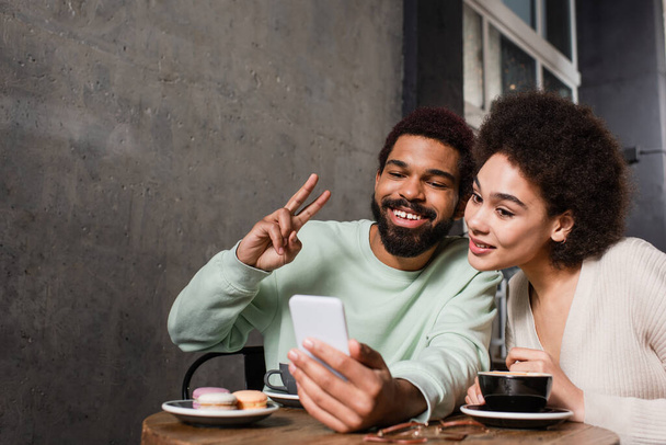 Smiling african american couple taking selfie on smartphone in cafe  - Fotó, kép