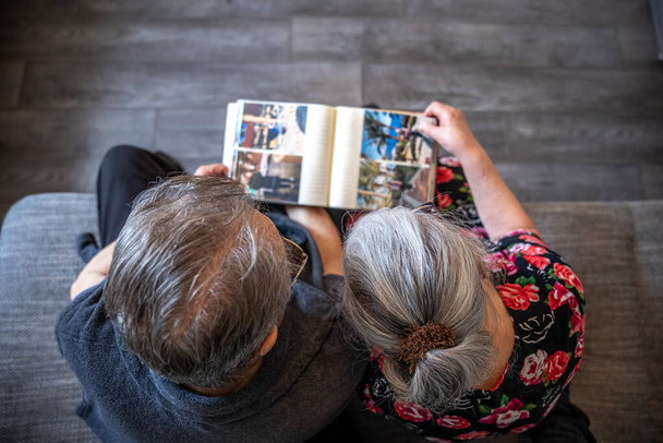 高齢者のカップルは、家族の写真アルバムを見ているトップビュー. - 写真・画像