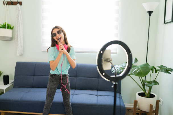 Leikkisä nuori tyttö aurinkolasit laulaa ja pelaa karaokea tallentaessaan videon lähettää hänen sosiaalisen median  - Valokuva, kuva