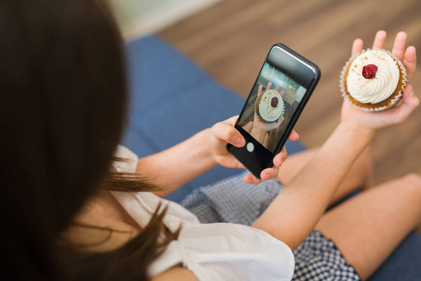 Persoonlijk perspectief van een influencer kind nemen van een foto met een smartphone om een lekkere cupcake te posten op haar sociale media - Foto, afbeelding