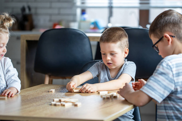 Small children play a board game with wooden cubes at home in the kitchen. - Zdjęcie, obraz