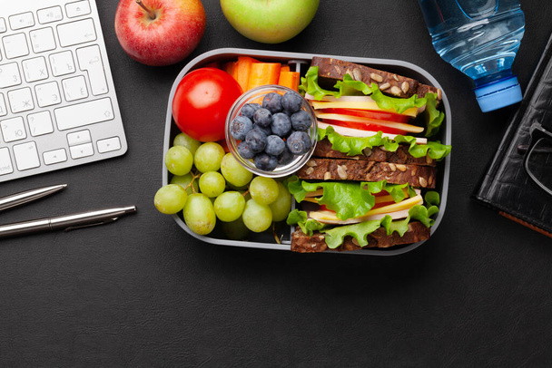 Healthy office lunch box with sandwich and fresh vegetables, water bottle, nuts and fruits on desk. Top view flat lay with copy space - Фото, зображення