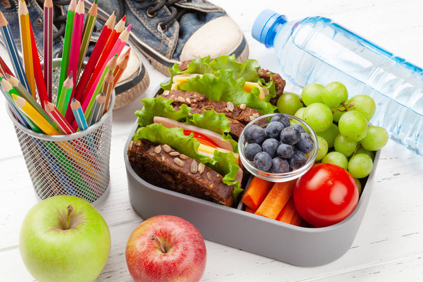 Здоровая школьная обеденная коробка с бутербродами и свежими овощами, бутылкой воды, орехами и фруктами - Фото, изображение