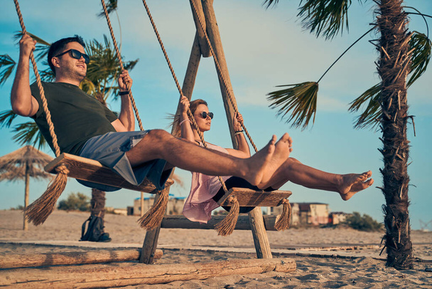 Joven pareja atractiva balanceándose en el balancín en la playa. - Foto, imagen