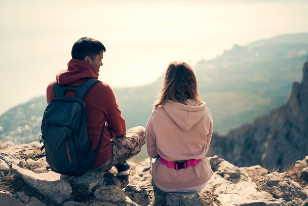Ζευγάρι κάθεται σε ένα βράχο, κοιτάζοντας το τοπίο και απολαμβάνοντας τη θέα και τον καθαρό αέρα. - Φωτογραφία, εικόνα