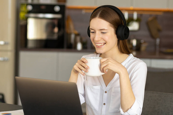 Happy young caucasian millennial girl in headphones uses laptop, talking on video conference, gesturing hand. Online communication concept - Φωτογραφία, εικόνα