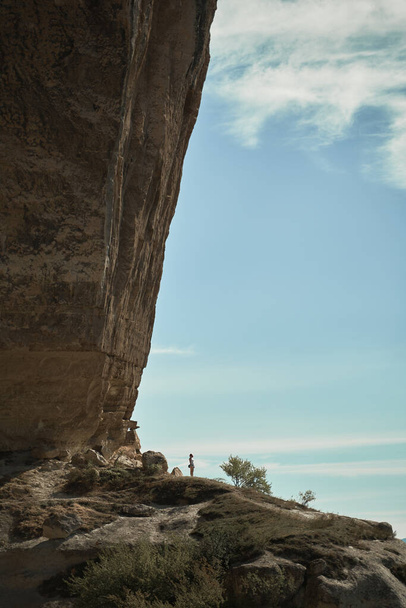 Genç bir kadın bir kayanın üzerinde kalır, manzaraya bakar ve manzaranın ve temiz havanın tadını çıkarır.. - Fotoğraf, Görsel