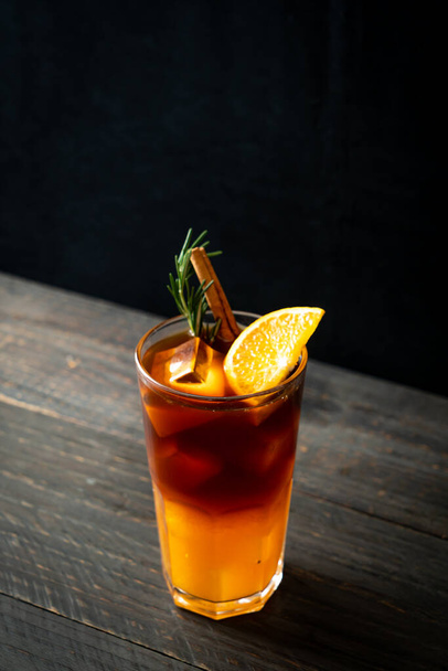 A glass of iced americano black coffee and layer of orange and lemon juice decorated with rosemary and cinnamon - 写真・画像