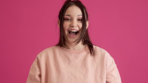 A happy young teenager girl is doing winner gesture while standing isolated over pink wall in the studio - Video