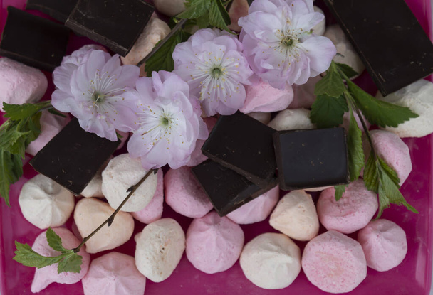 Op een roze bord staan stukjes pure chocolade, snoep en amandelbloemen.  - Foto, afbeelding