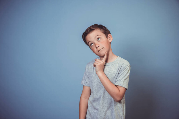 cool, young boy with grey t-shirt is posing in front of blue background in the studio  - Φωτογραφία, εικόνα