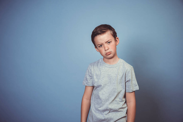 cool, young boy with grey t-shirt is posing in front of blue background in the studio  - Photo, Image