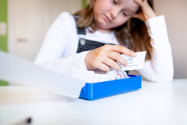 pretty young schoolgirl sitting on her desk in her room at home learning english vocabulary using flashcards during corona time - Fotografie, Obrázek