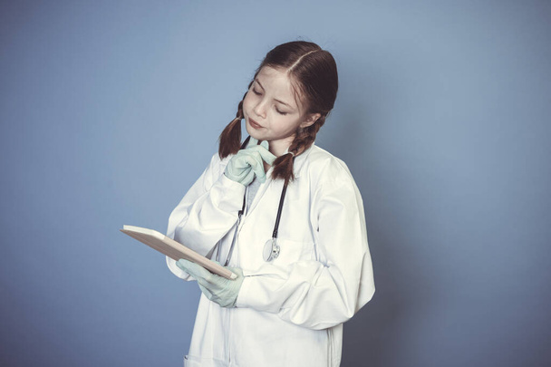 beautiful young girl dressed as doctor with green gloves and digital tablet in front of blue background - Foto, immagini