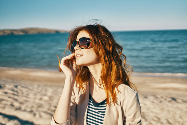 donna con i capelli rossi e occhiali da sole ride in natura sulla spiaggia vicino al mare - Foto, immagini