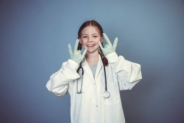 young girl dressed as doctor with green rubber gloves and stethoscope in front of blue background - Foto, immagini