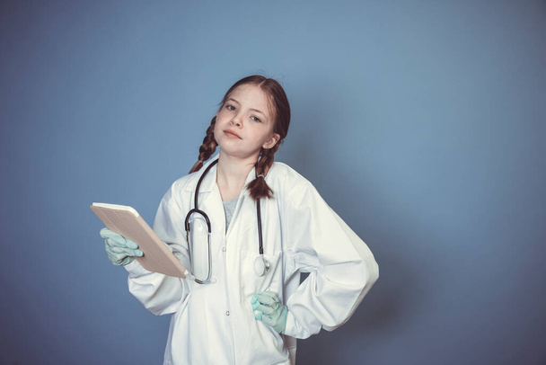 beautiful young girl dressed as doctor with green gloves and digital tablet in front of blue background - Foto, immagini
