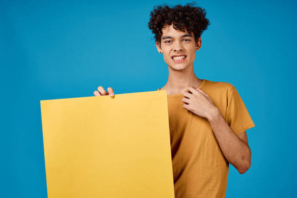 Χαρούμενος τύπος με σγουρά μαλλιά κίτρινη αφίσα mockup μπλε φόντο - Φωτογραφία, εικόνα