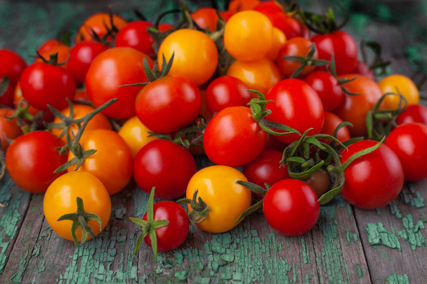 Tomato background. Fresh red, yellow and orange tomatoes with green tails on a wooden background. Summer harvest of homemade vegetables. - Valokuva, kuva