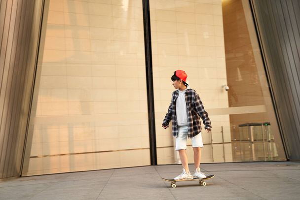 quince años de edad adolescente asiático niño monopatín en frente de moderno edificio - Foto, Imagen