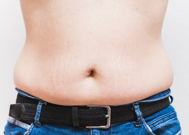 The belly and navel of an unrecognizable fat man wearing blue jeans and a black belt - Photo, Image