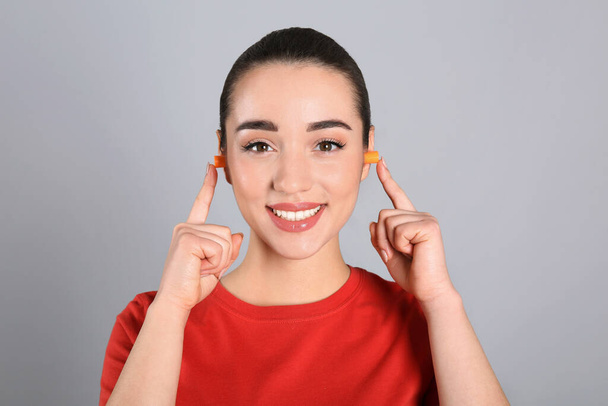 Young woman inserting foam ear plugs on grey background - Zdjęcie, obraz