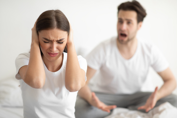 Nešťastná žena zakrývá uši, zatímco rozzlobený manžel křičí v ložnici - Fotografie, Obrázek