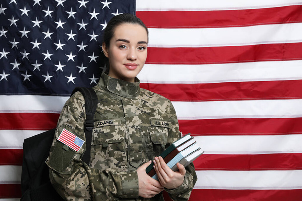 Female soldier with backpack and books near flag of United States, space for text. Military education - Zdjęcie, obraz