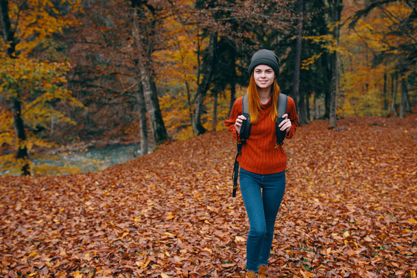 Traveler with a backpack in the autumn forest and hat sweater jeans fallen leaves lake trees - Foto, Imagen