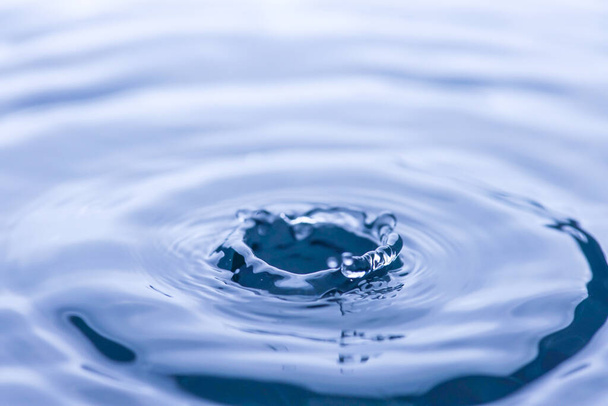 ガラスの青い色の水に水滴が飛び散って水を反射しています. - 写真・画像