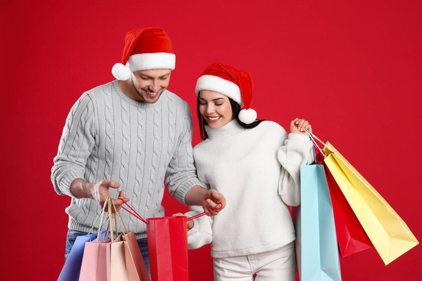 Happy couple with paper bags on red background. Christmas shopping - Foto, Imagen