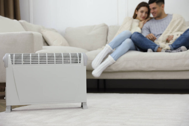 Electric heater and couple on sofa at home - Foto, Bild