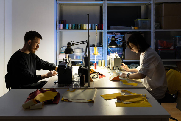 Fiatal ruhatervezők dolgoznak. Férfi- és női professzionális szabók varrógépekre varrva - Fotó, kép