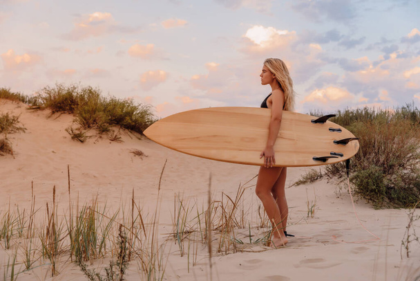 Surfermädchen mit Surfbrett am Strand und warmen Farben des Sonnenuntergangs. Attraktive Surferinnen am Strand - Foto, Bild