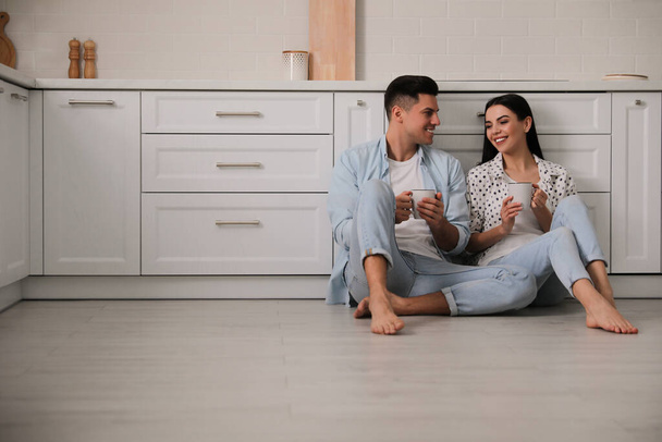 Happy couple sitting on warm floor in kitchen. Heating system - Photo, image
